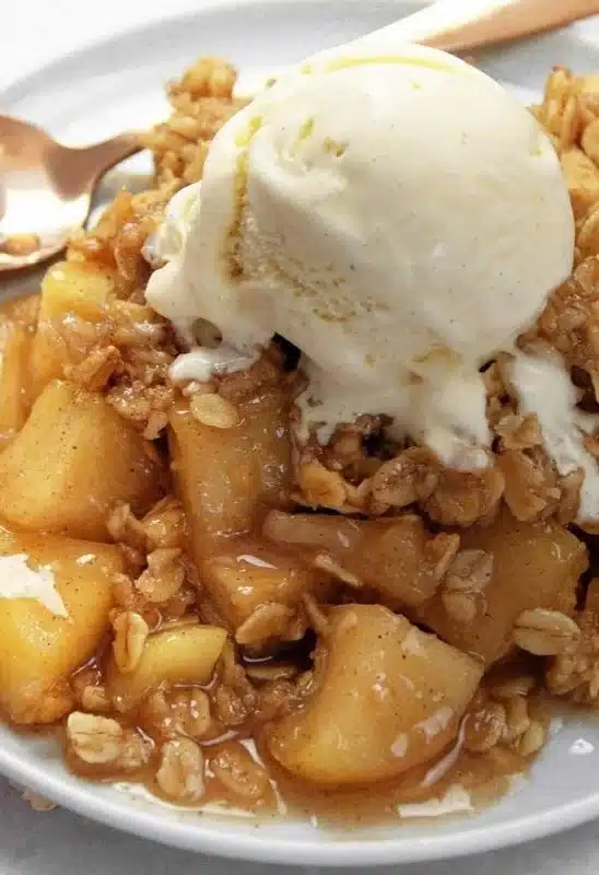 Gluten free apple crumble served in a dish with a scoop of vanilla ice cream on top