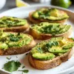 Mini avocado toasts appetizers topped with fresh ingredients on a wooden platter.
