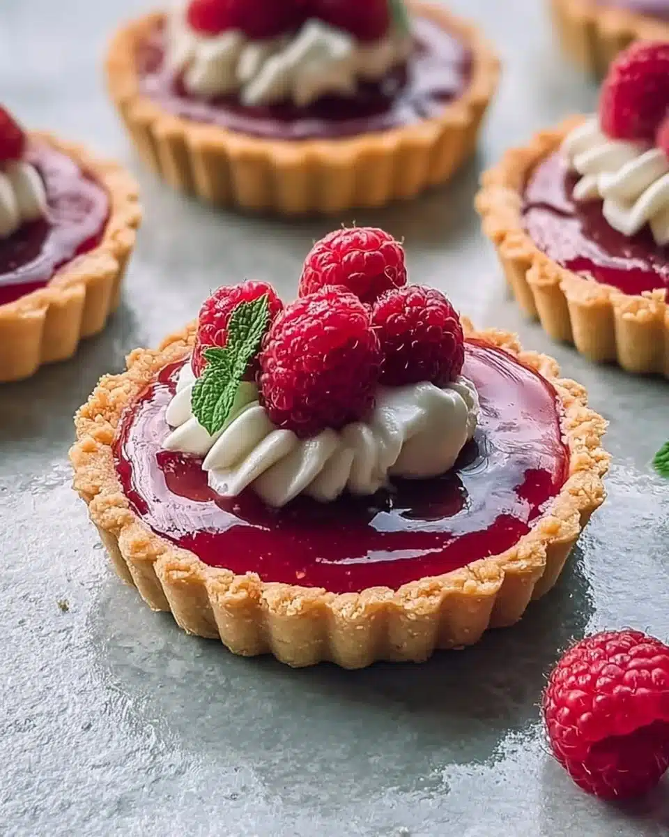 Vegan raspberry curd tarts garnished with fresh raspberries and mint leaves
