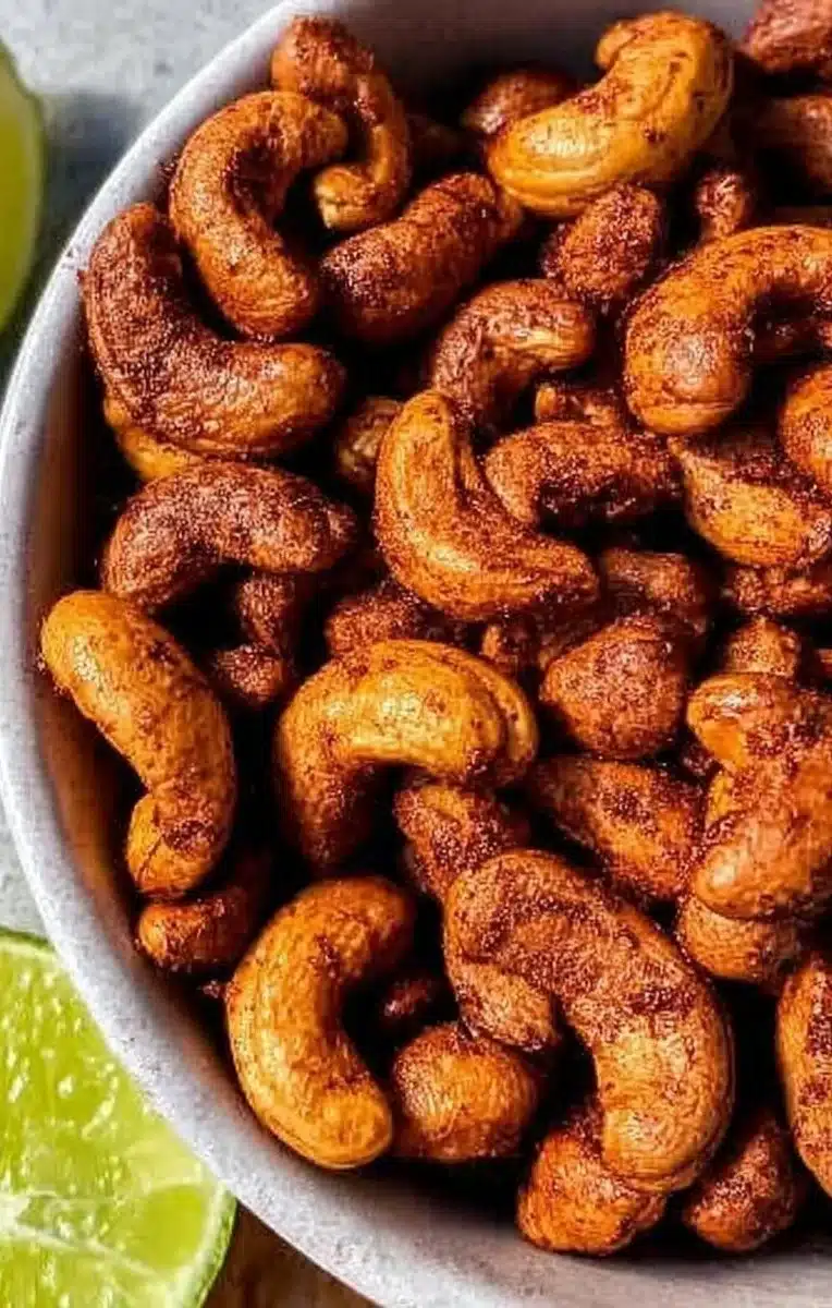 A bowl of spicy Chili Lime Cashews on a wooden table, showcasing their vibrant flavor.