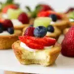 Fruit cheesecake sugar cookie cups topped with fresh fruit and cream