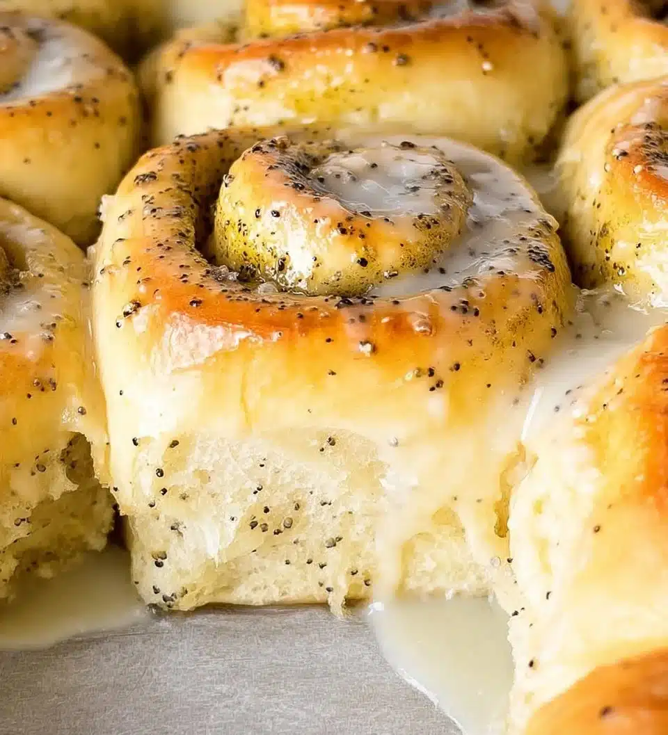 Fluffy lemon poppy seed rolls on a plate with lemon slices and poppy seeds