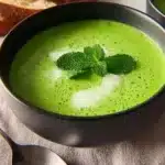 A bowl of vibrant green pea and mint soup garnished with fresh mint leaves.
