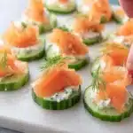 Smoked salmon cucumber bites on a platter, garnished with fresh herbs.