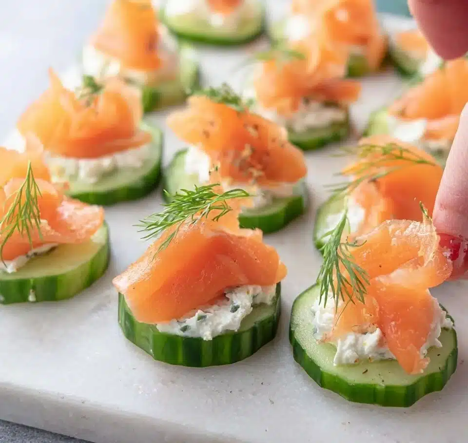 Smoked salmon cucumber bites on a platter, garnished with fresh herbs.