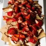 Plate of strawberry nachos topped with cream and chocolate drizzle