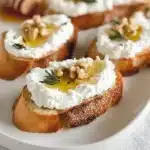 Whipped ricotta crostini topped with honey and fresh herbs on a wooden board.