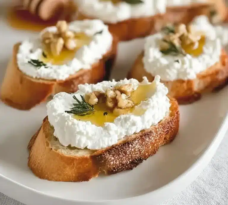 Whipped ricotta crostini topped with honey and fresh herbs on a wooden board.