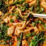 A bowl of chicken curry noodles garnished with fresh herbs and spices.