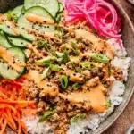 Healthy ground turkey rice bowls topped with fresh vegetables and sauce