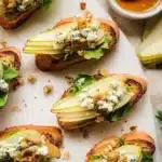Delicious pear and blue cheese crostini topped with fresh herbs on a wooden board.