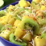 A vibrant bowl of pineapple kiwi salad garnished with mint leaves