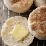 Freshly baked sourdough English muffins on a wooden cutting board.