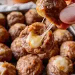 Plate of cheesy meatballs with melted cheese and marinara sauce.