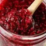 Homemade raspberry jam in a jar with fresh raspberries nearby