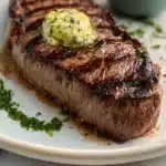Steak topped with delicious herb butter on a plate, garnished with fresh herbs