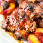 Delicious Bourbon Peach BBQ Chicken on a grill with vibrant peaches and sauce.