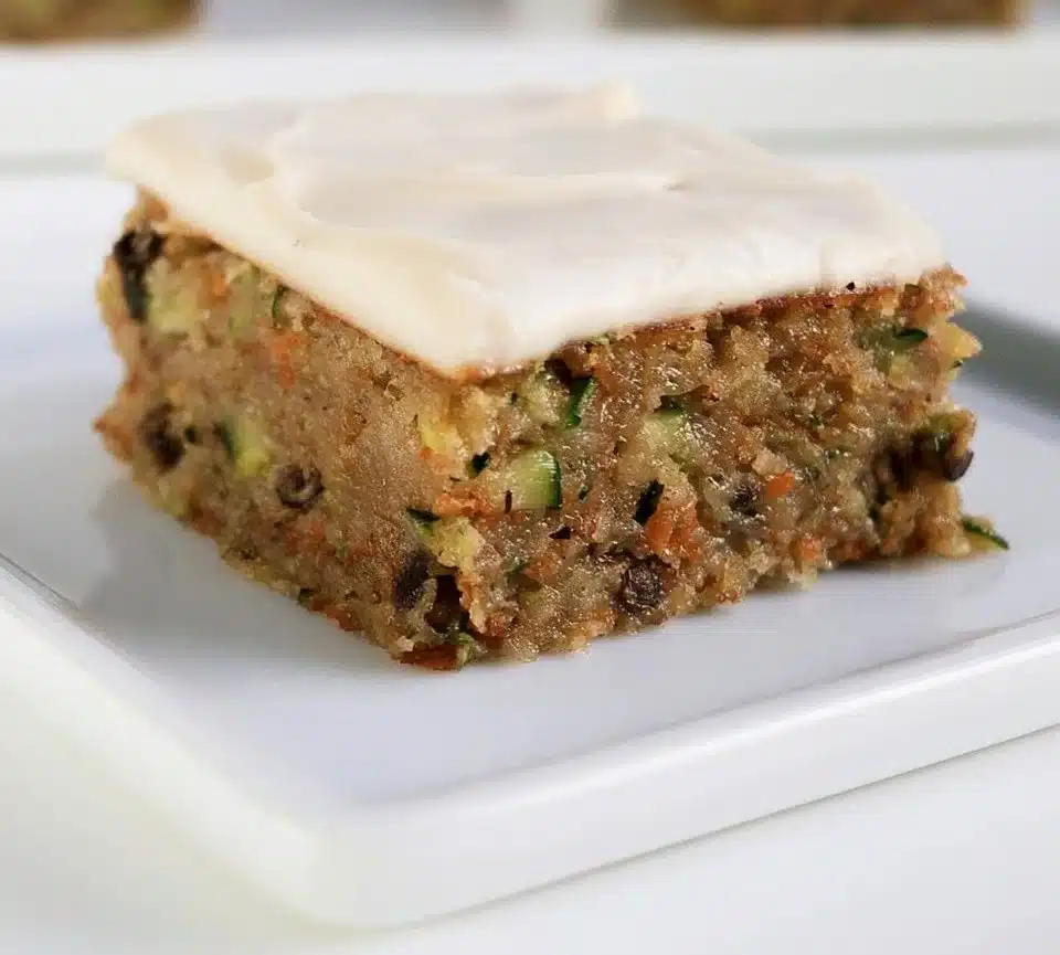 Freshly baked zucchini bars topped with nuts and frosting on a wooden table.